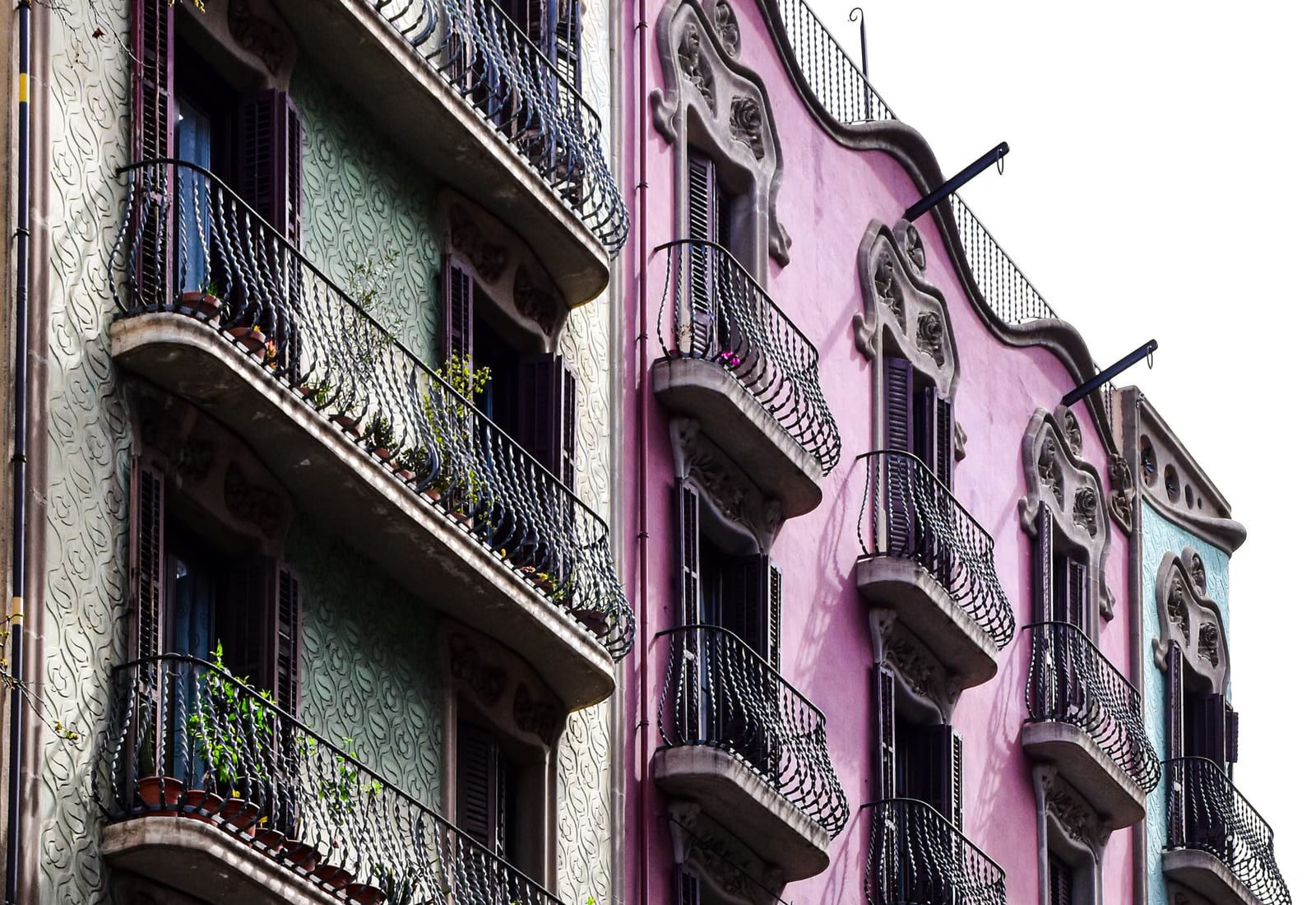 Fachadas de edificios del centro de Barcelona con balcones de hierro forjado pintadas en tonos rosa y verde