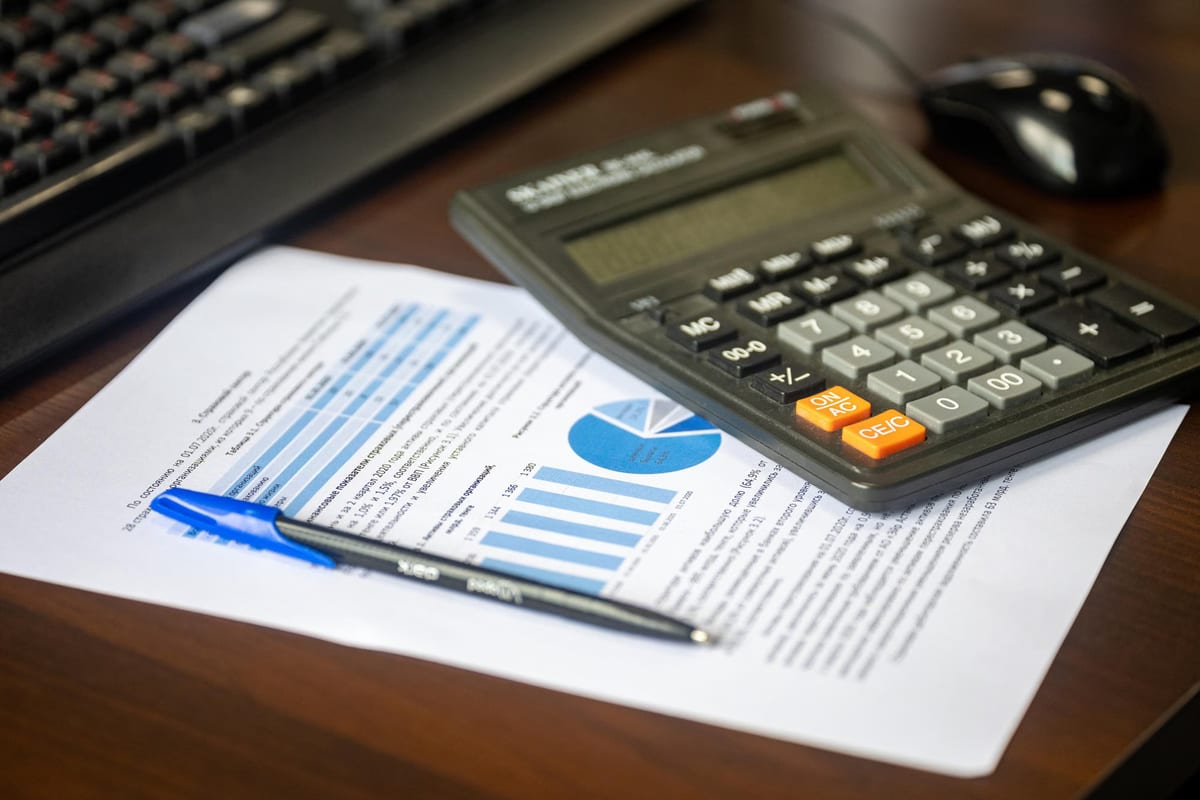 Calculadora, bolígrafo y documentos con gráficos impresos sobre una mesa de despacho