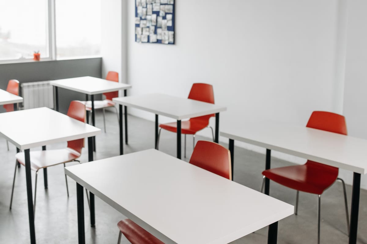 Aula vacía con mesas blancas y sillas rojas dispuestas en filas