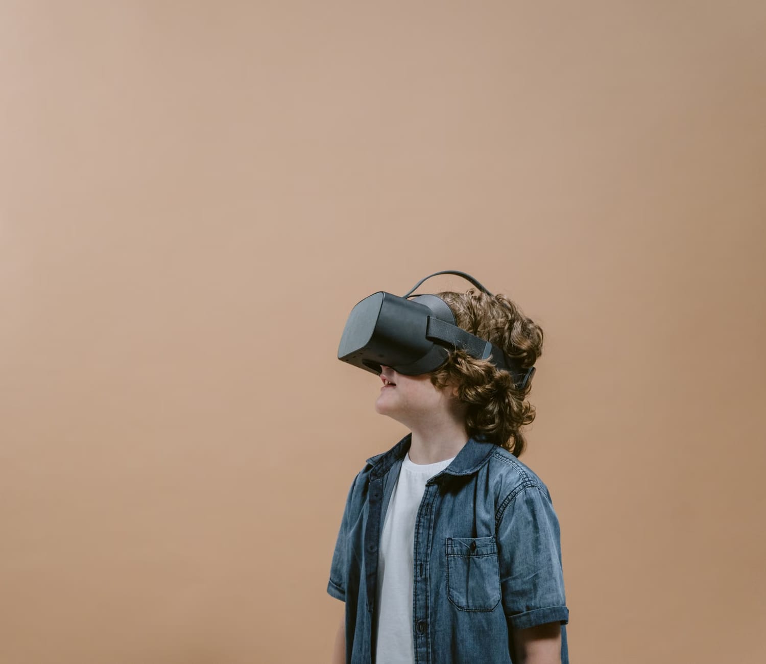 Un niño de perfil, con un visor de realidad virtual puesto, sobre un fondo liso