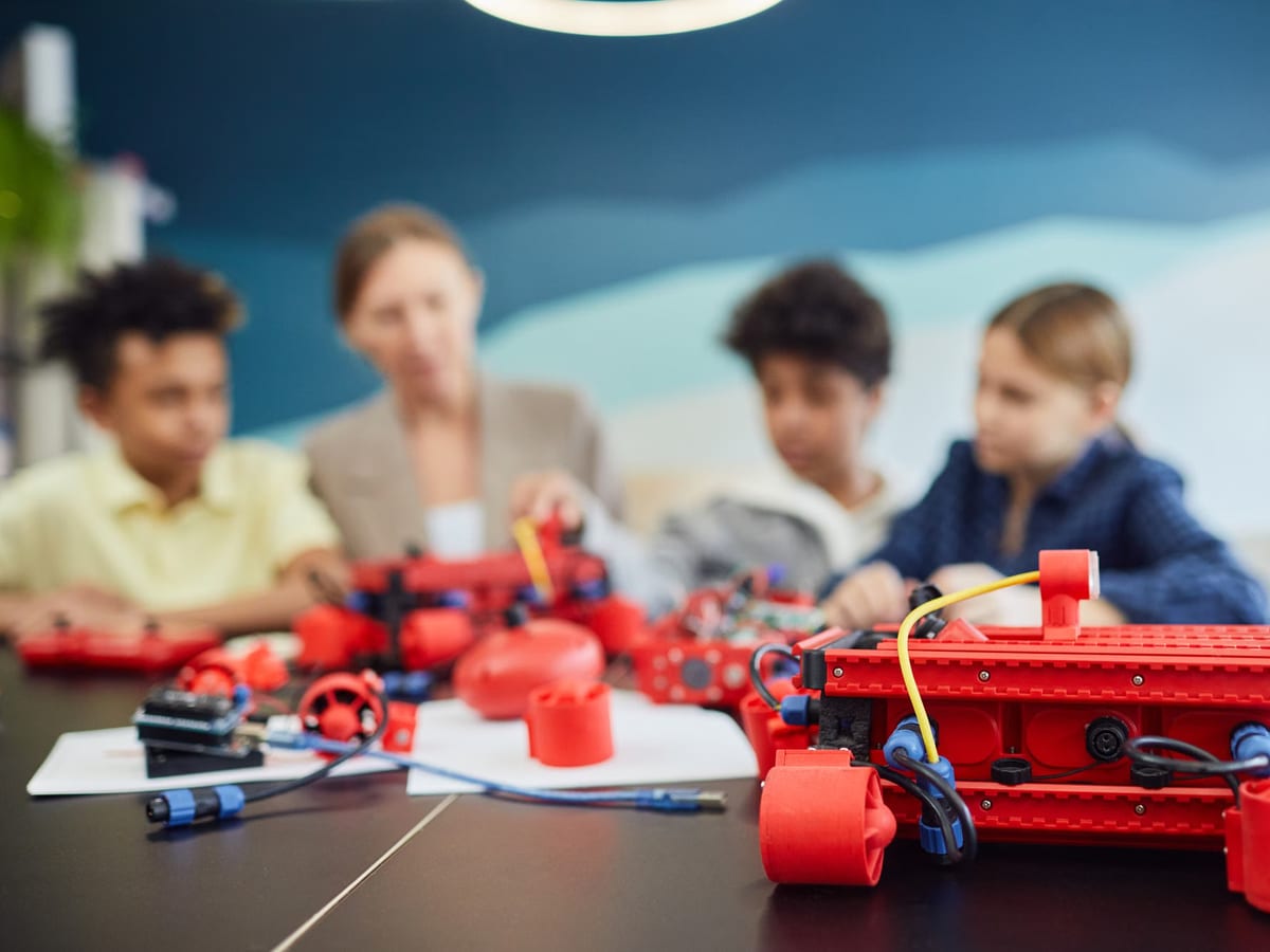 Alumnado y docentes montando kits de robótica de piezas rojas alrededor de una mesa