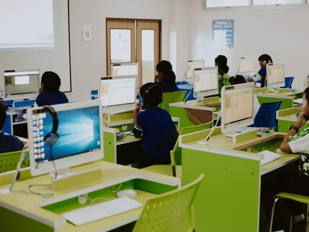 Aula de informática con filas de mesas y monitores encendidos mientras el alumnado trabaja