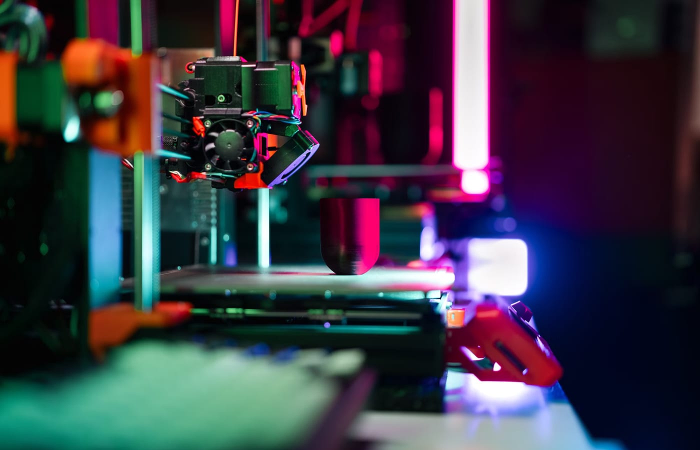Impresora tridimensional en funcionamiento en un taller de prototipos, iluminada con luces de colores